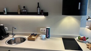 Una cocina moderna con un lavaplatos de acero inoxidable, una placa de inducción Bosch, un extractor de aire negro y una estantería de madera para especias.