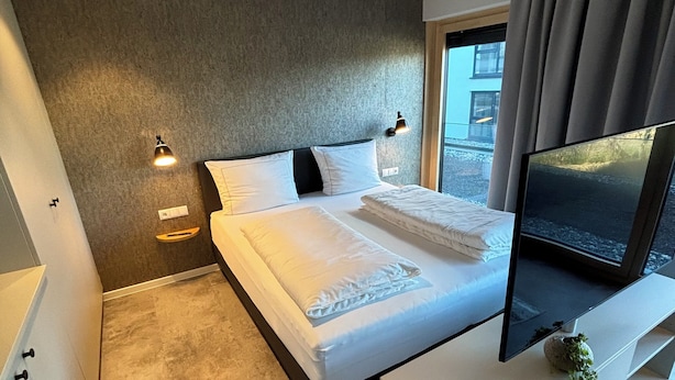 Un dormitorio moderno con cama, lámparas de noche, televisión y vistas al exterior.