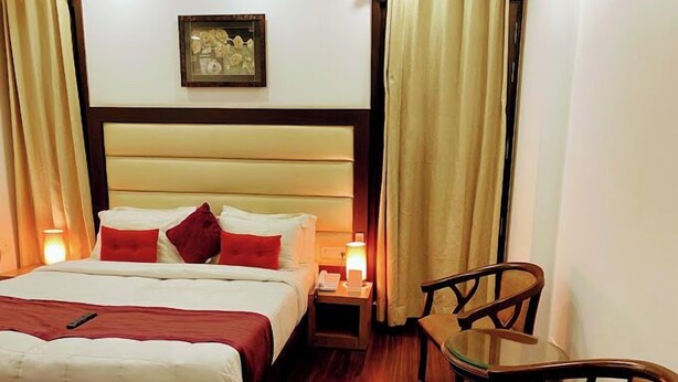 A hotel room with a bed, bedside table, lamp, chair, and a painting on the wall. - Indiyaah Residency (Gurugram)