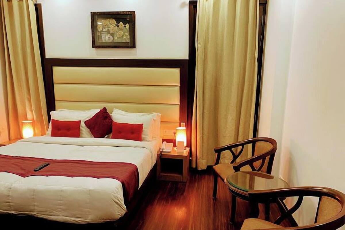 A hotel room with a bed, bedside table, lamp, chair, and a painting on the wall.