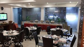 A conference room with round tables, black office chairs, a red tablecloth-covered table, a clock on the wall, and a television displaying a sports game. - Indiyaah Residency (Gurugram)
