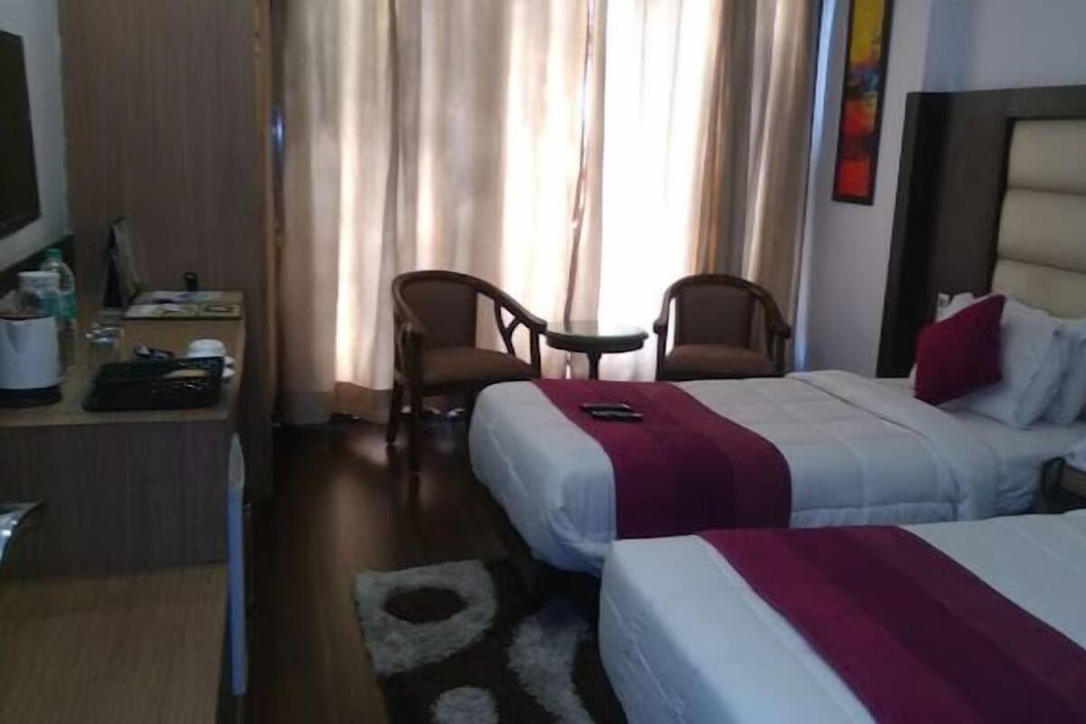 A hotel room with two beds, a desk with a chair, a small table, and a TV.