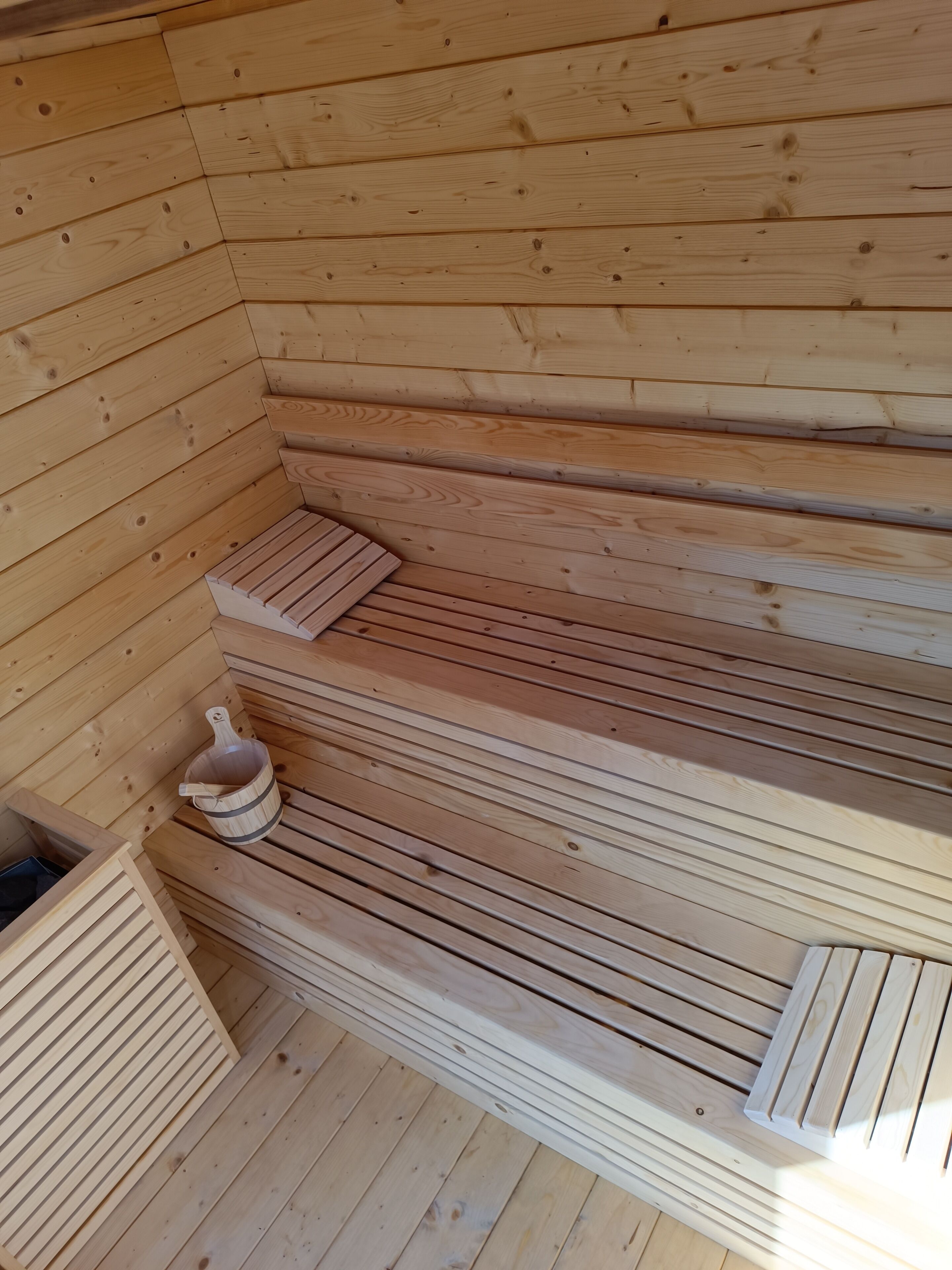 Un sauna avec des bancs en bois et un seau en bois.
