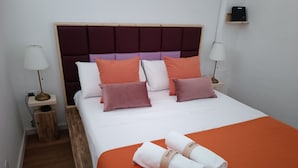 Ein ordentlich bezogenes Bett mit orangefarbener Bettdecke, weißen und orangefarbenen Kissen und zwei gerollten Handtüchern.