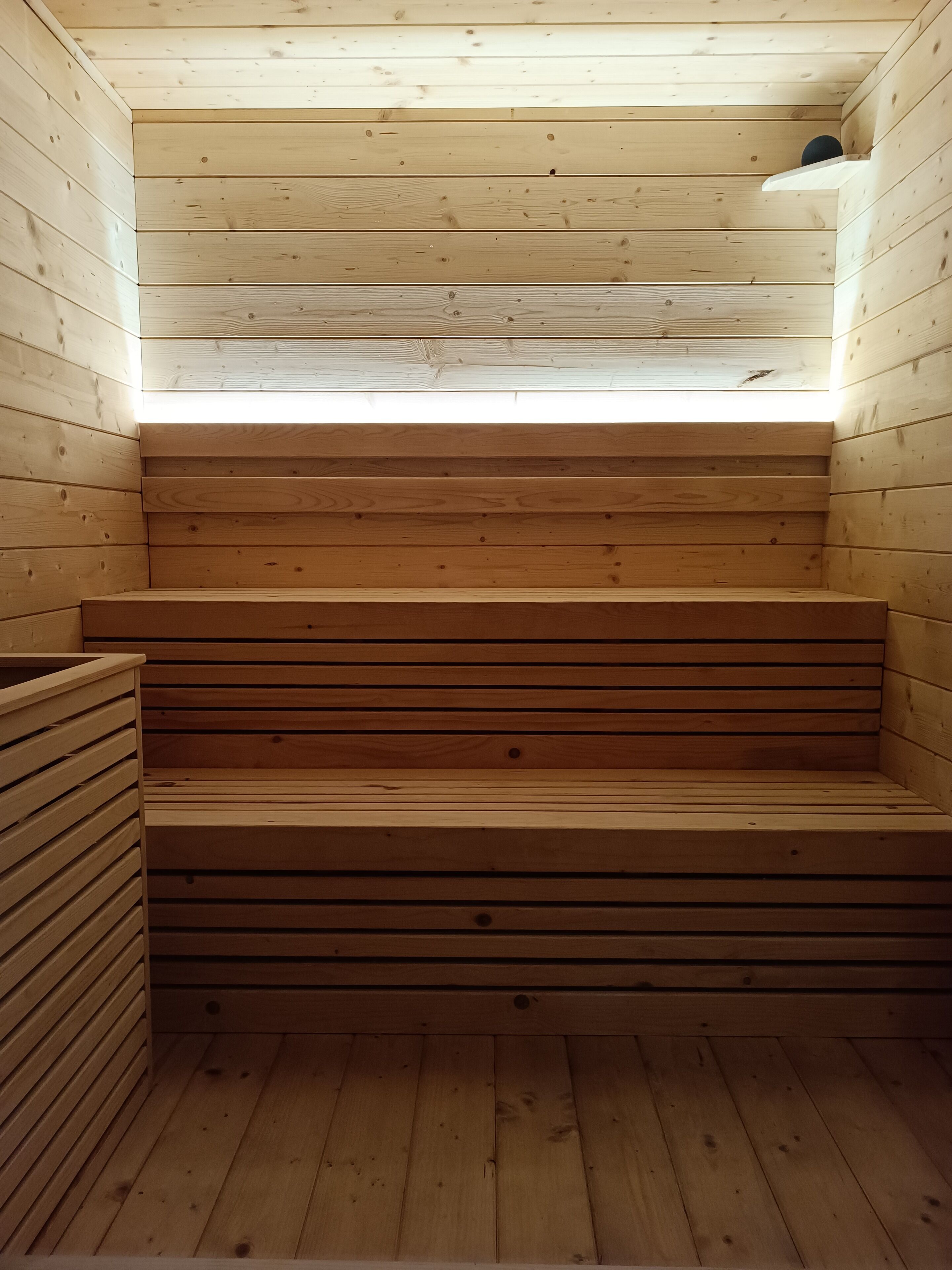A wooden sauna with a sloped ceiling and a small window at the top.