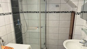 Ett badrum med en dusch som är avskärmad med glasväggar, ett vitt handfat och kaklade väggar.