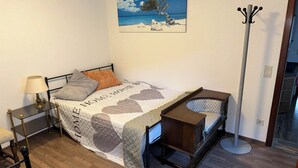 Ett sovrum med en säng, ett nattduksbord, en lampa och en klädhängare.