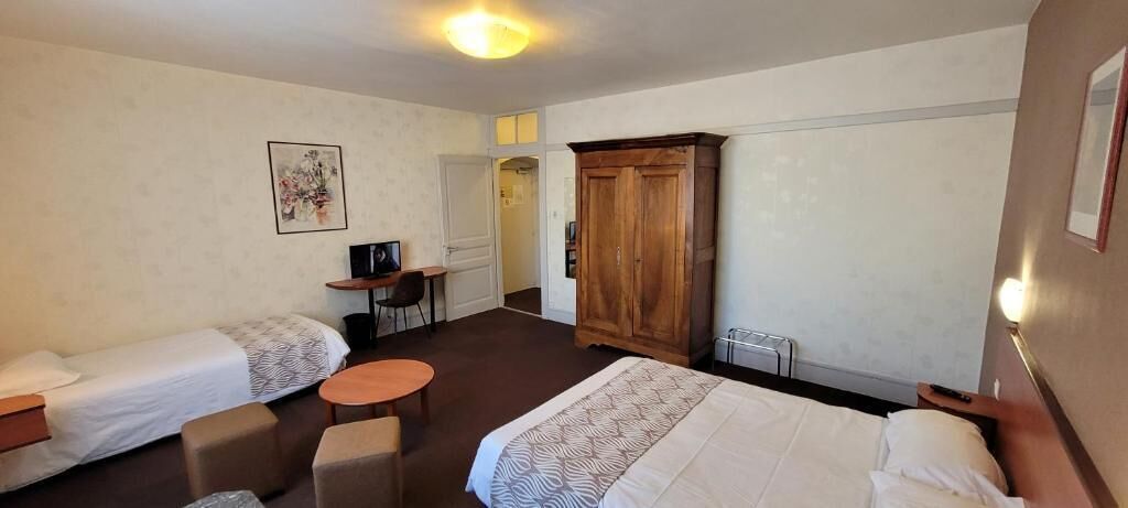 Una habitación de hotel con dos camas individuales, una mesita redonda pequeña, un armario y un escritorio con una silla.