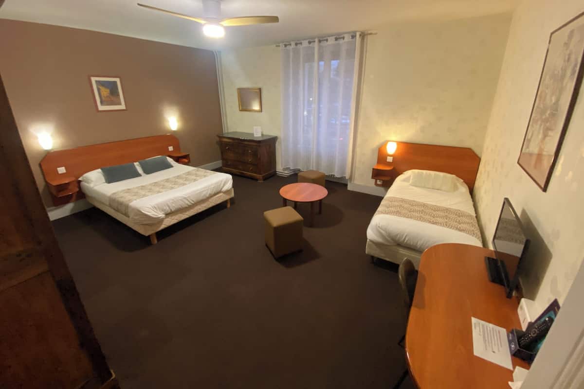 Une chambre d’hôtel avec deux lits, une petite table, une chaise, une commode et un ventilateur de plafond.