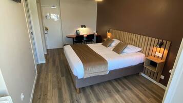 Une chambre d’hôtel équipée d’un lit, d’un bureau, d’une chaise, d’un ventilateur de plafond et d’une table de chevet.