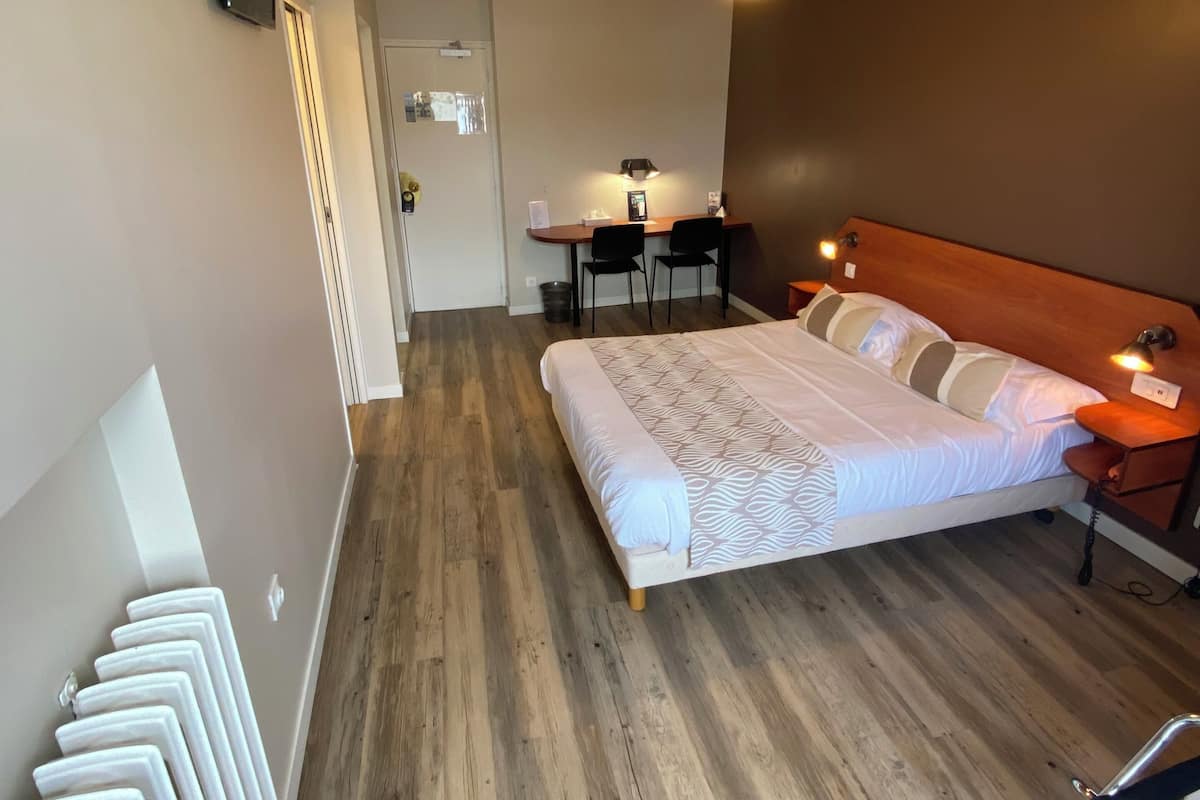 A hotel room with a bed, a desk with two chairs, a ceiling fan, and a TV mounted on the wall.