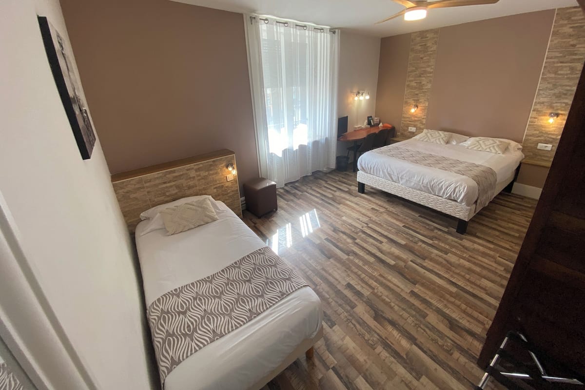 Une chambre d’hôtel avec deux lits, un ventilateur de plafond, un bureau avec une chaise et une fenêtre avec des rideaux.