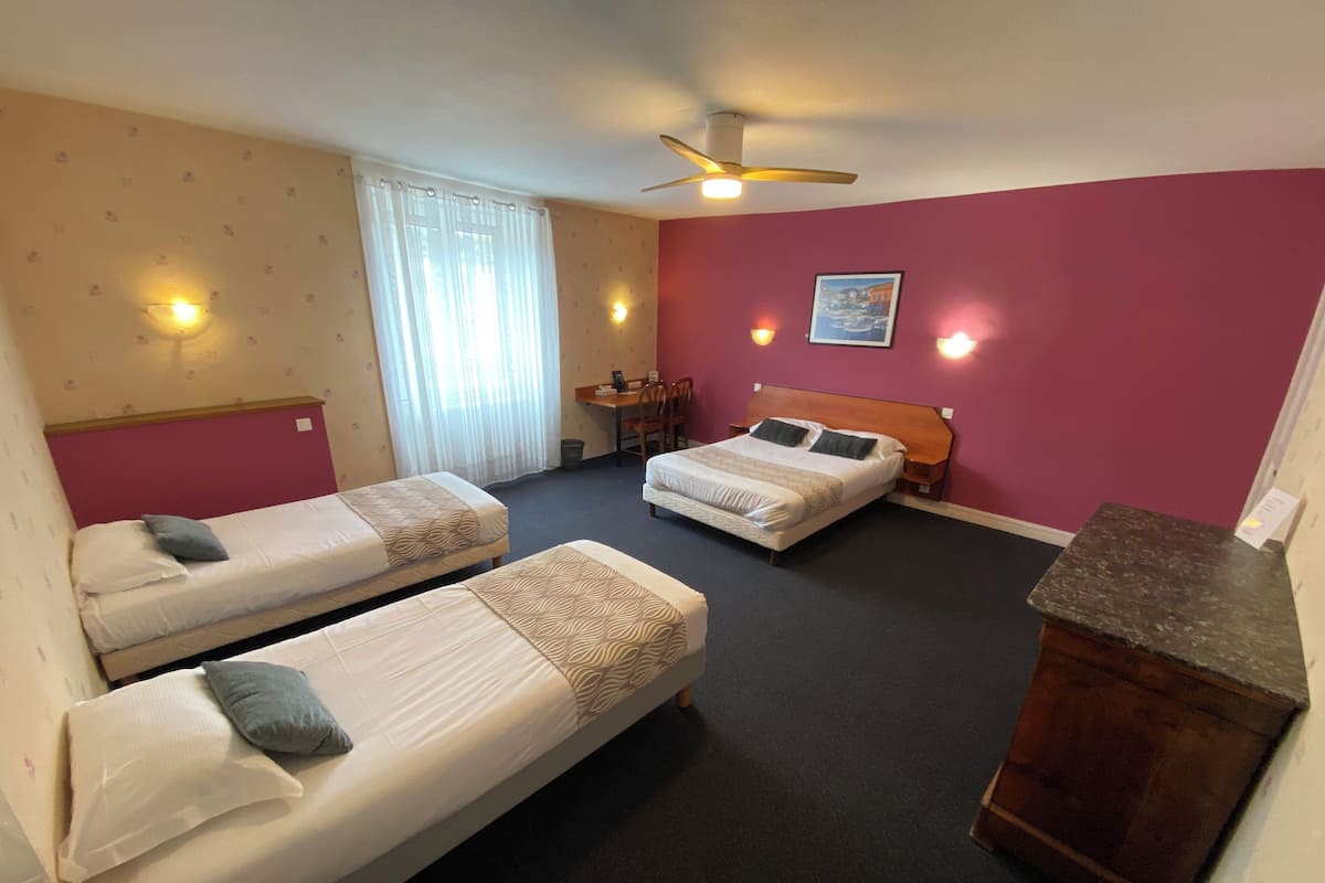 Une chambre d’hôtel avec deux lits simples, un bureau, une chaise, une armoire en bois et un ventilateur de plafond.