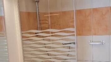 A bathroom with a glass shower enclosure, a wooden vanity with a sink, and tiled walls.