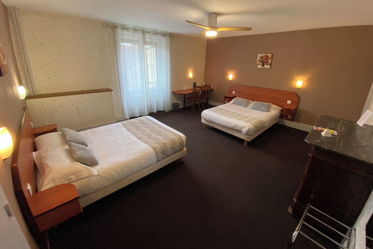 Une chambre d’hôtel avec deux lits, un bureau, une chaise, un ventilateur de plafond et une petite table.
