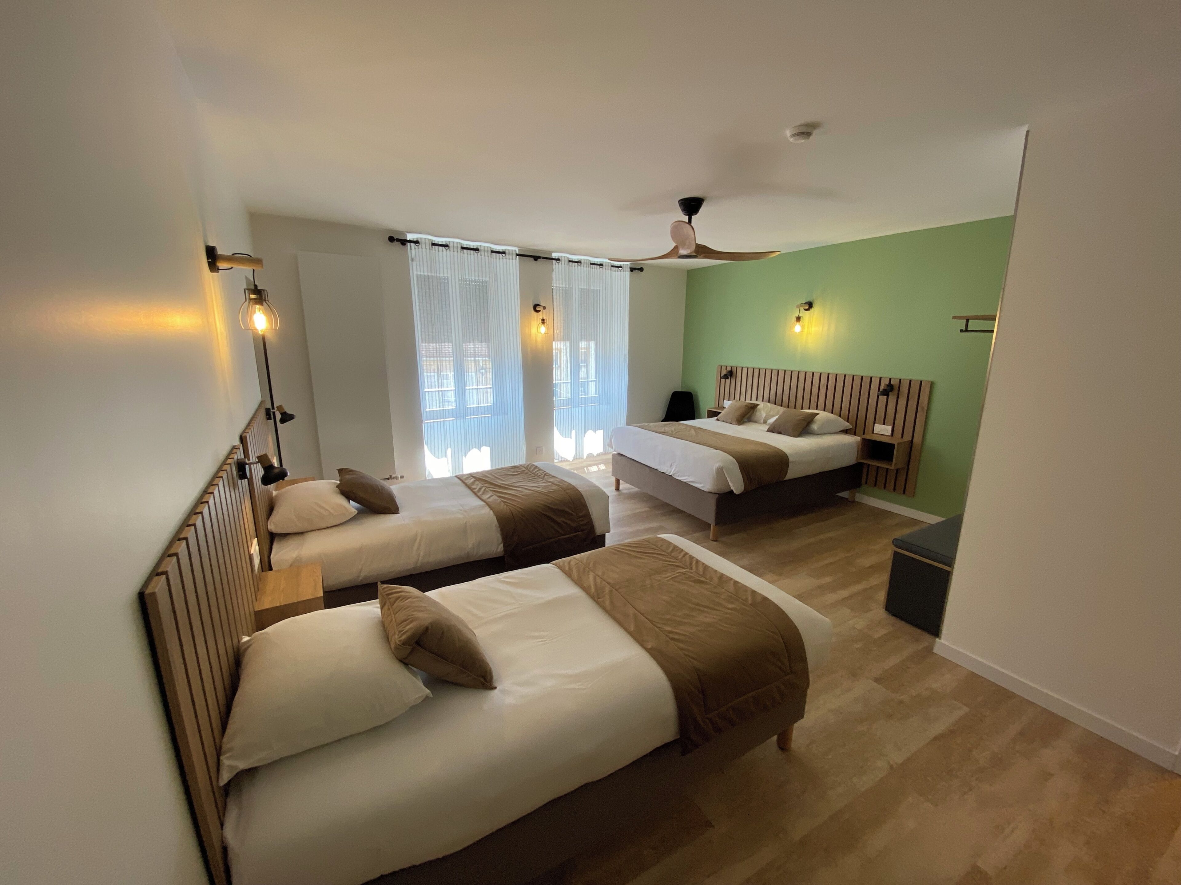Habitación de hotel con dos camas, ventilador de techo y ventana con cortinas.