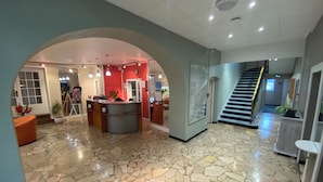 A lobby with a reception desk, a staircase, and a tiled floor. - NOUVEL HOTEL  (Lons-le-Saunier)