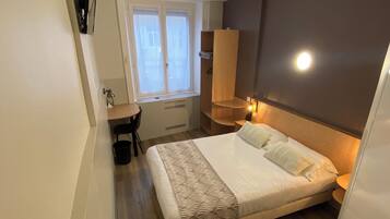 A bedroom with a bed, a desk, a chair, a window, and a wardrobe.