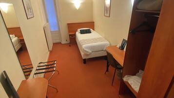 Una habitación de hotel funcional con cama, escritorio, silla, armario y una mesita.