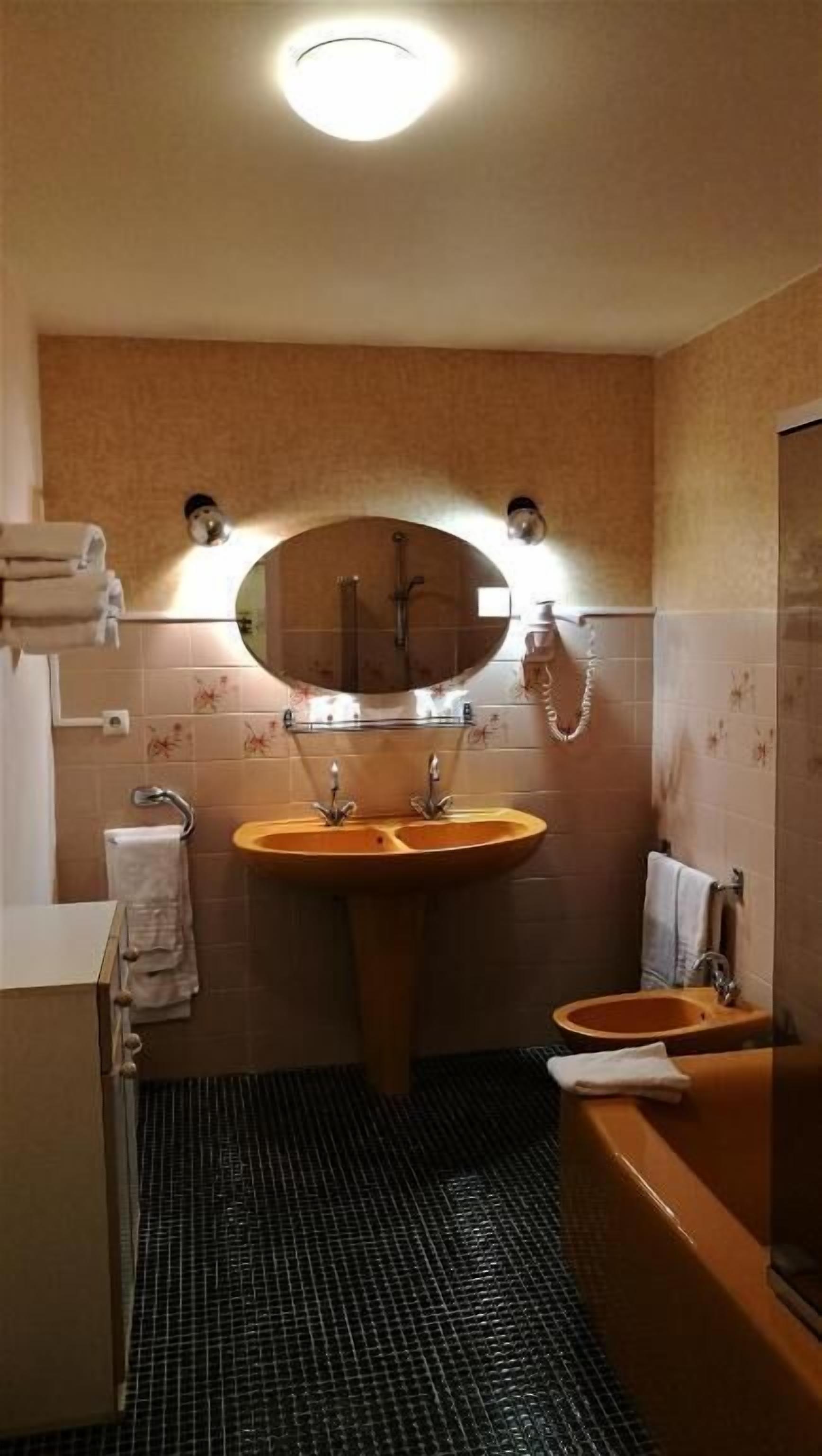 Une salle de bain avec un grand miroir rond, deux lavabos, une baignoire et une douche.