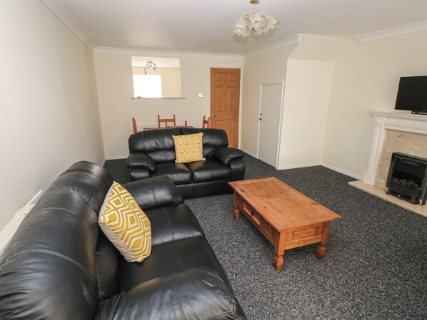 A living room with a black leather sofa, a wooden coffee table, a fireplace, and a television. - 21 Heol Gylfinir (Barry)