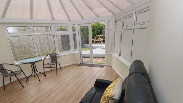 Een glazen veranda met een zwarte bank, een klein tafeltje en twee stoelen.