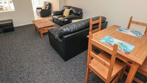 Een gemeubileerde woonkamer met een bank, fauteuil, salontafel en een houten eettafel.