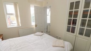 Een slaapkamer met een bed, twee ramen, een radiator en een inbouwkast met geëtste glazen deuren.