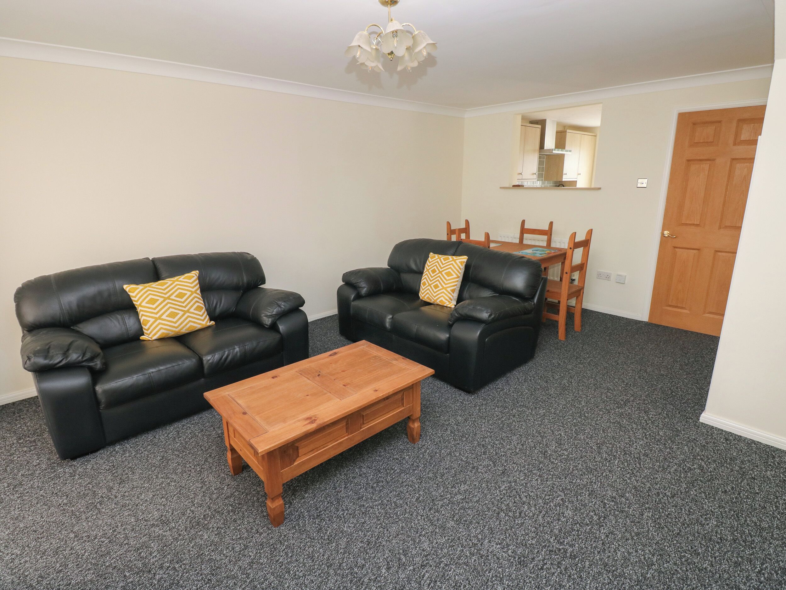 A living room with two black leather sofas, each with a patterned cushion, a wooden coffee table, and a dining table with chairs in the background.