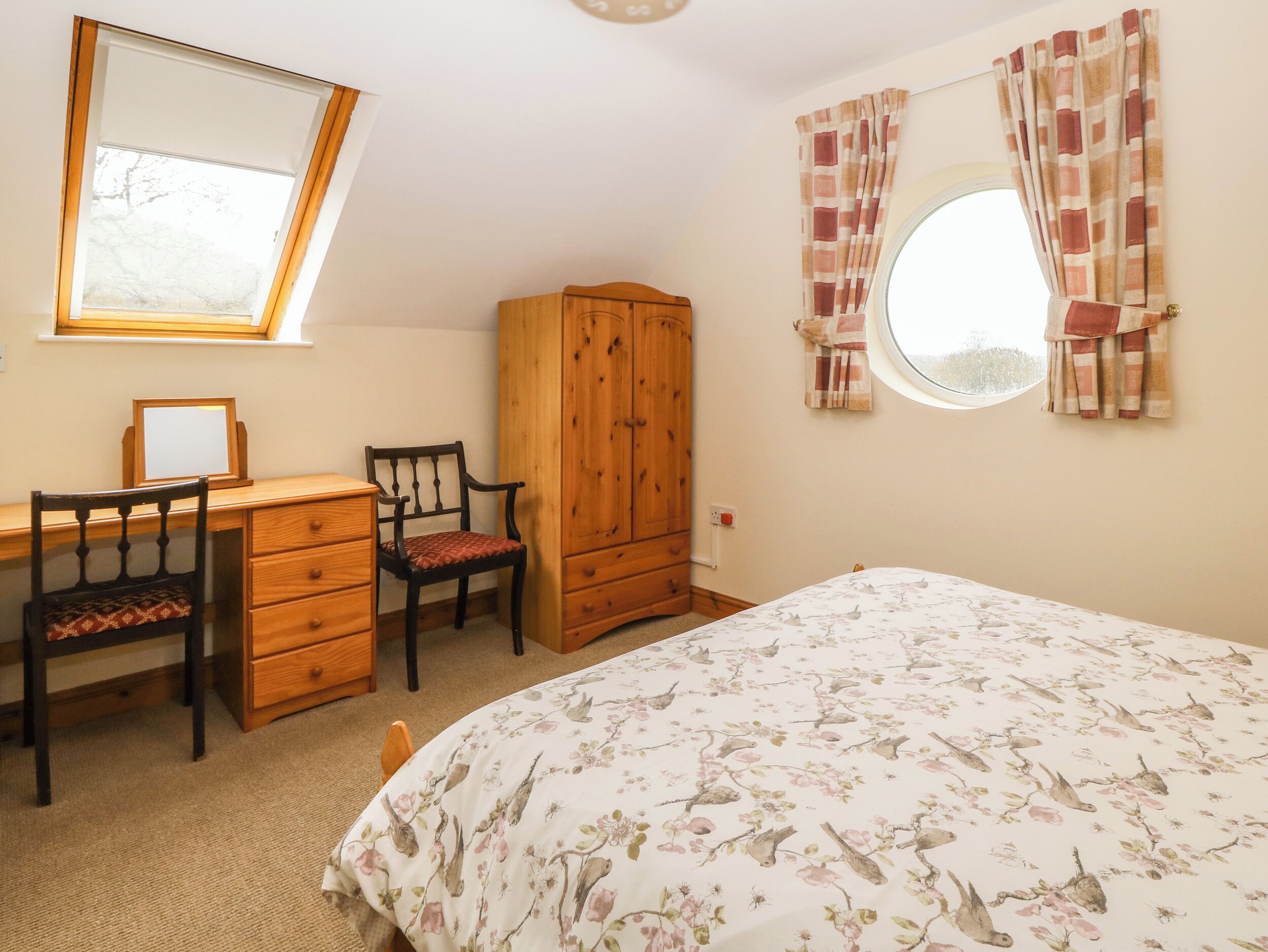 A bedroom with a bed, a desk, a chair, a wardrobe, a mirror, and a window with curtains.