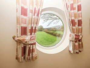 A window with a view of a green landscape and bare trees. - Meadow View (Caernarfon)