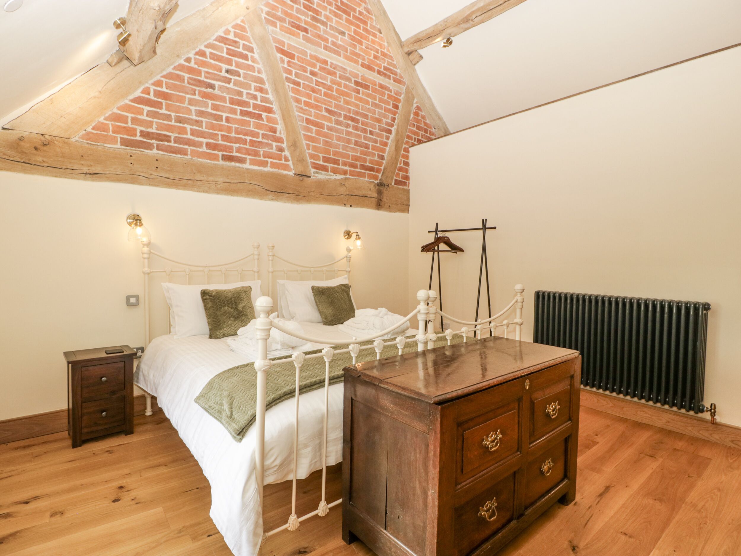 A bedroom with a bed, wooden dresser, and a brick wall.
