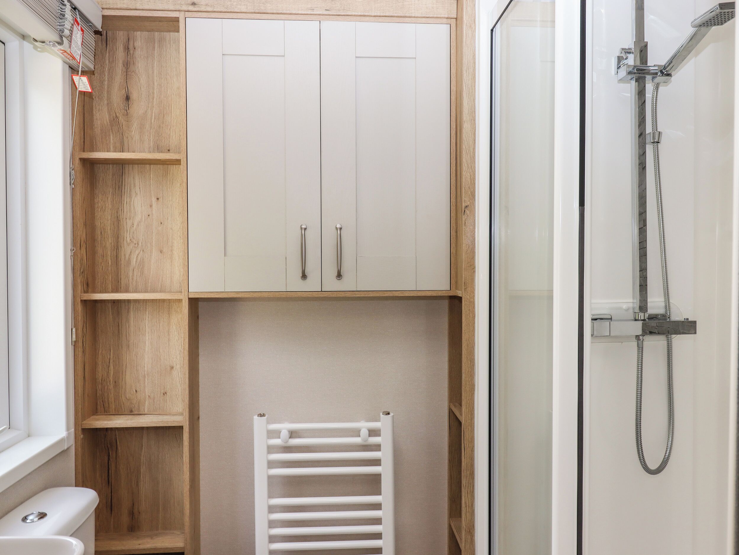 A bathroom with a shower, toilet, and a wooden cabinet with two drawers.