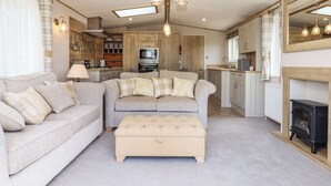 A cozy living room with a sofa, ottoman, and a kitchen area in the background. - Ambleside (Cullompton)