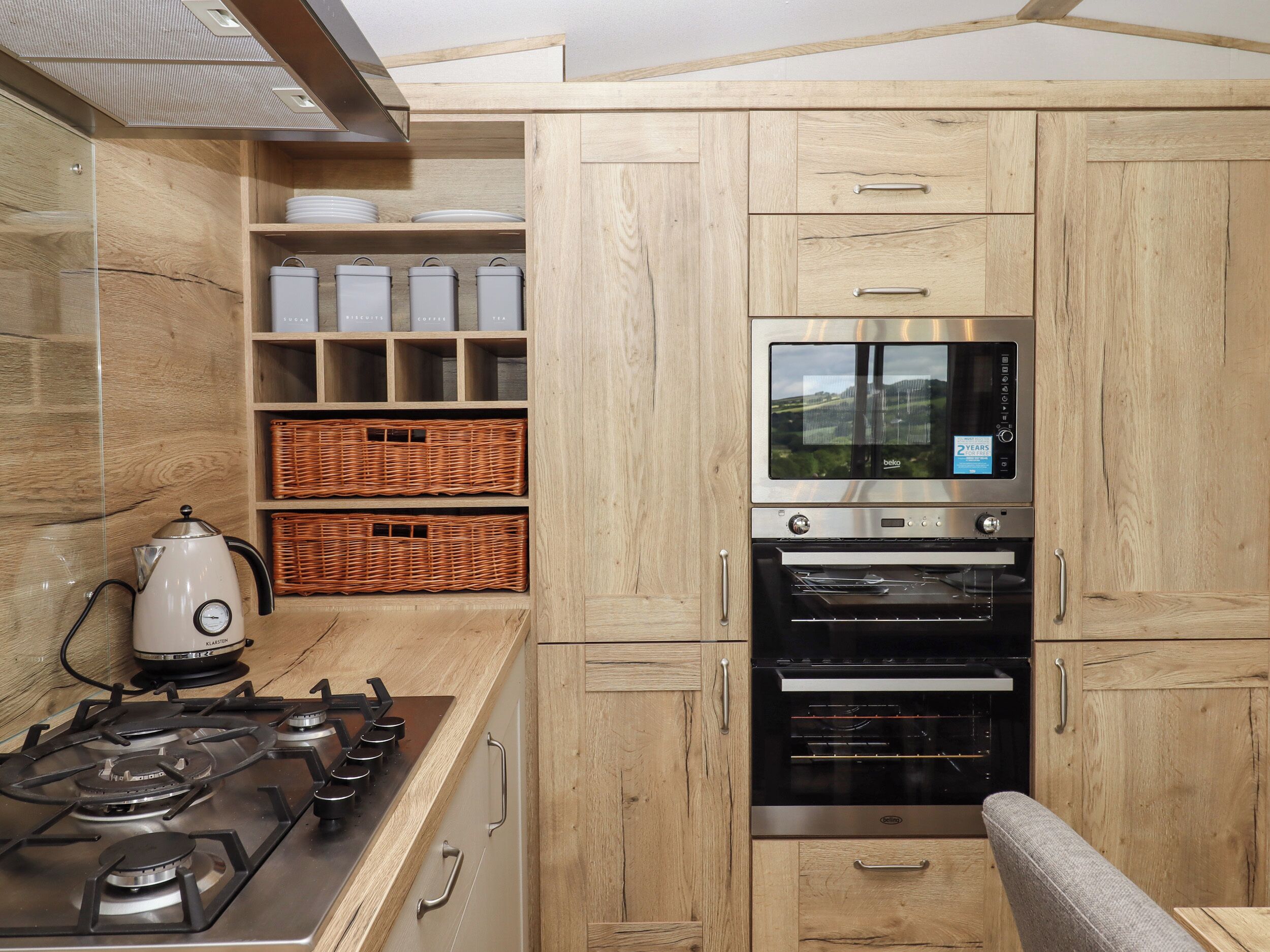 A modern kitchen with wooden cabinets, a built-in oven, a stove, and wicker baskets.