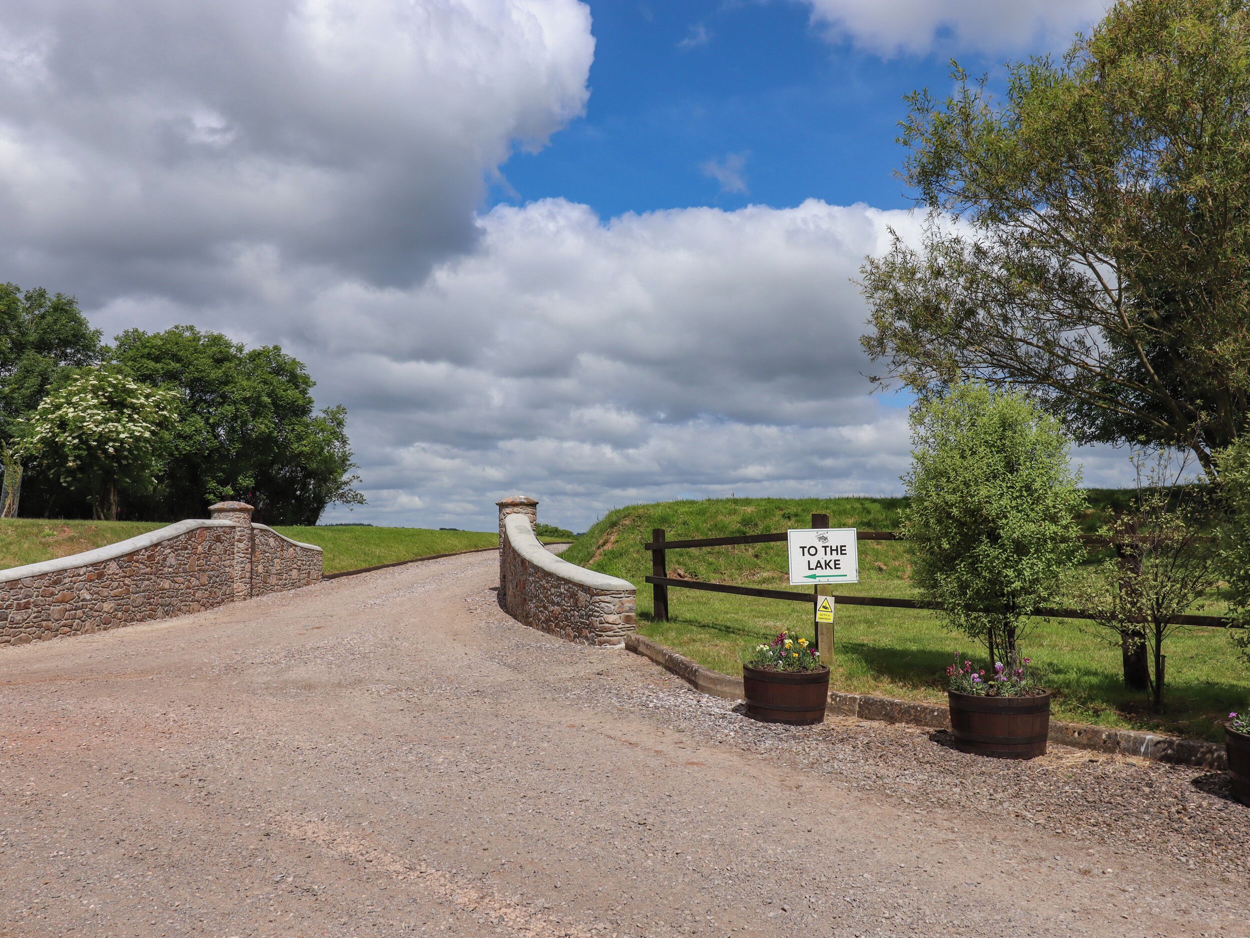 A gravel path leading to a stone wall with a sign reading "TO THE LAKE".