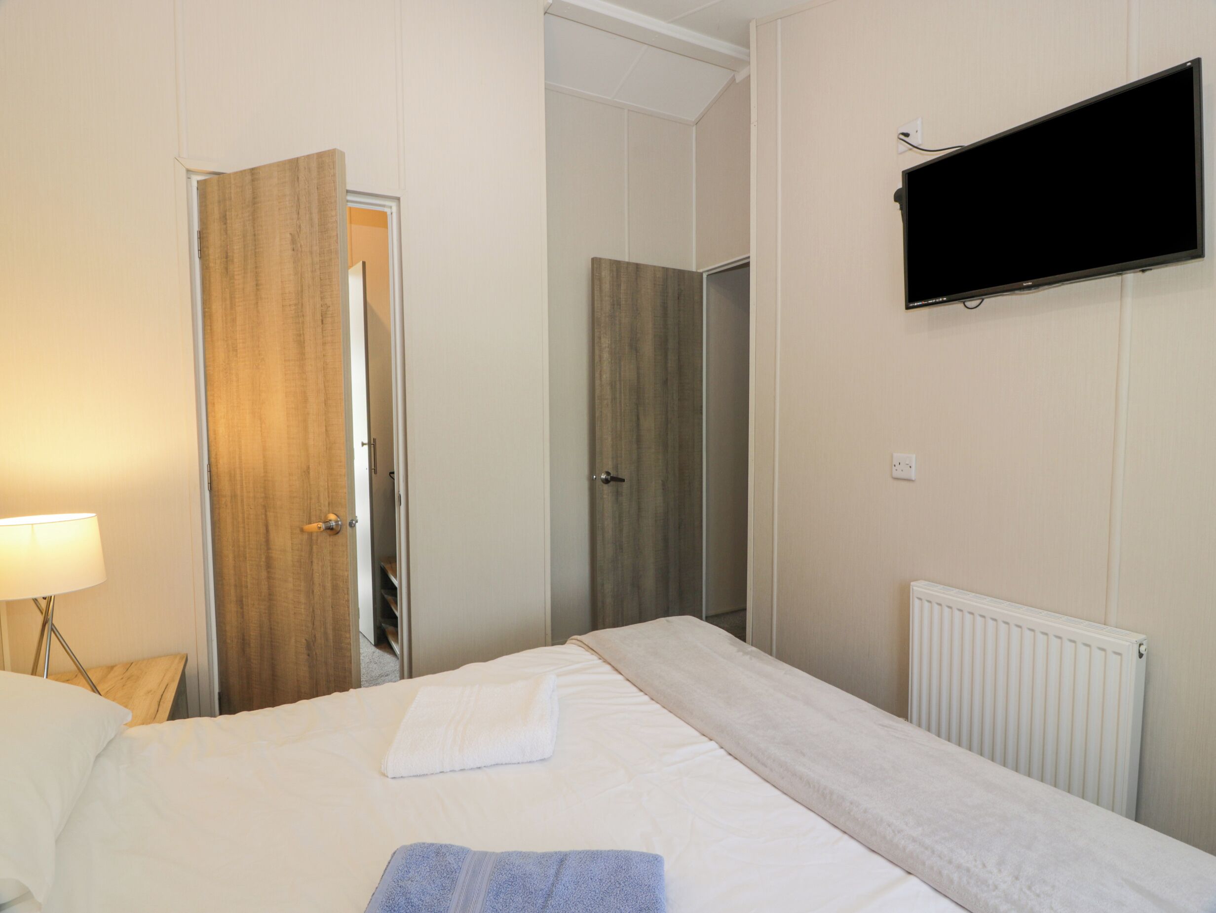 A hotel room with a bed, a TV mounted on the wall, a door leading to a bathroom, and a radiator.