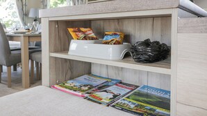 Un espace de vie chaleureux avec une étagère en bois contenant des collations, une poubelle et des magazines de voyage.
