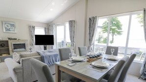Un espace repas moderne avec une longue table dressée pour six personnes, des chaises à revêtement gris et un téléviseur à écran plat fixé au mur.