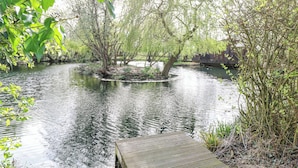 A wooden dock extending into a calm river surrounded by lush greenery and trees. - Heron Lodge (Bury St Edmunds)