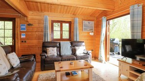 A cozy cabin interior with a wooden ceiling, a leather sofa, a wooden coffee table, and a television on a wooden stand. - Heron Lodge (Bury St Edmunds)