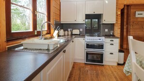 A compact kitchen with white cabinets, a sink, a stove, and an oven. - Heron Lodge (Bury St Edmunds)