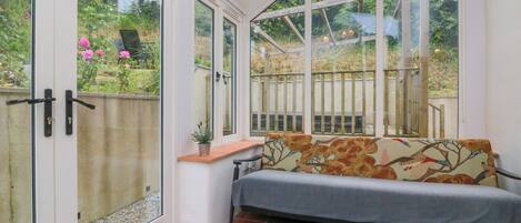 A conservatory with a bench, a small table, and a view of a garden.