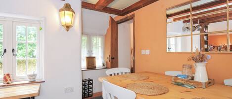 Un coin repas avec une table en bois, des chaises blanches et une étagère fixée au mur où sont rangés des ustensiles de cuisine.