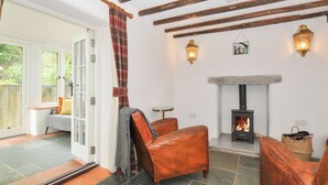 A cozy room with a stone fireplace, leather armchairs, and a view through a glass door. - Rose Cottage (Okehampton)