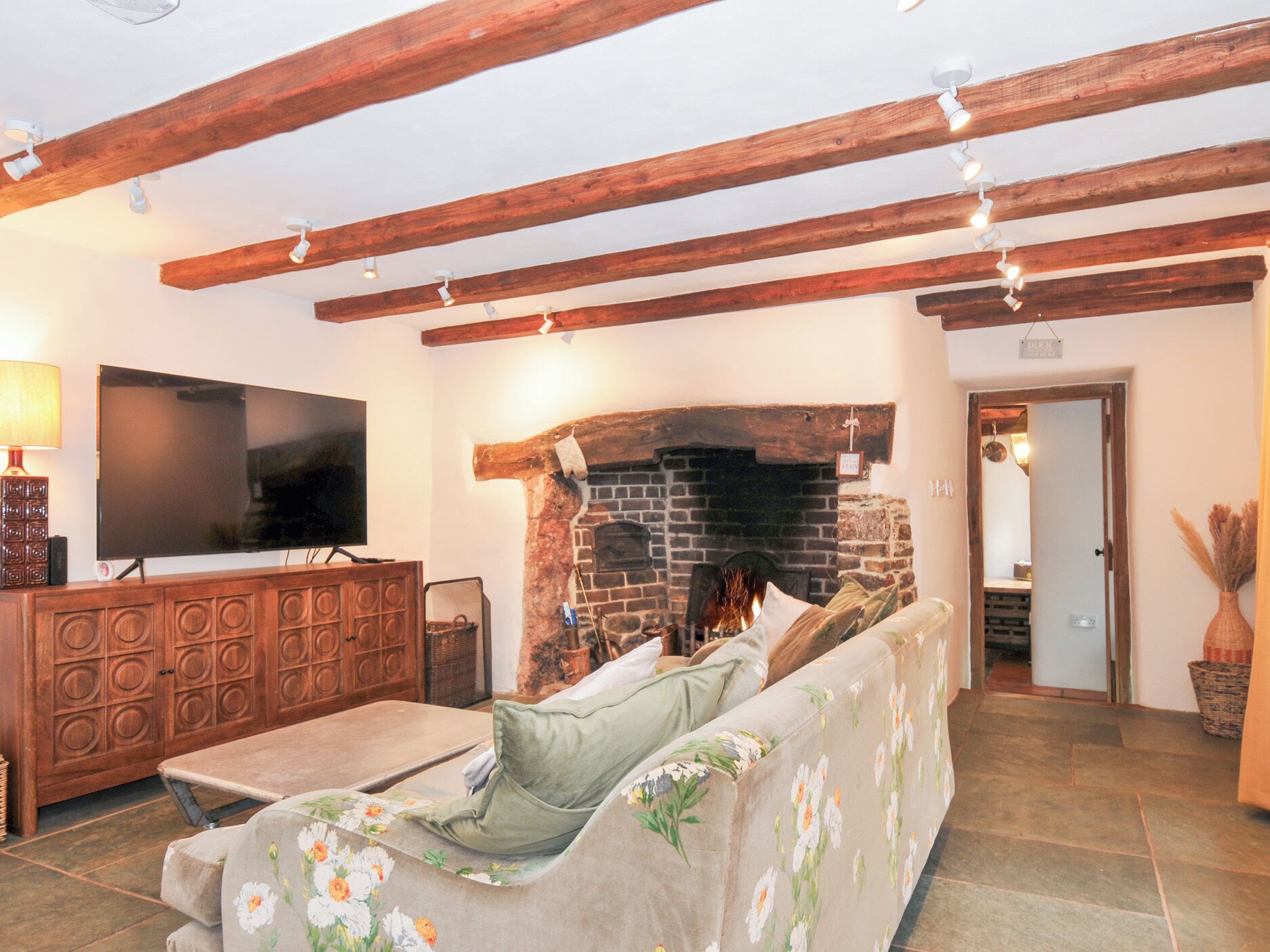 A living room with exposed wooden beams, a fireplace, a television, and a sofa.