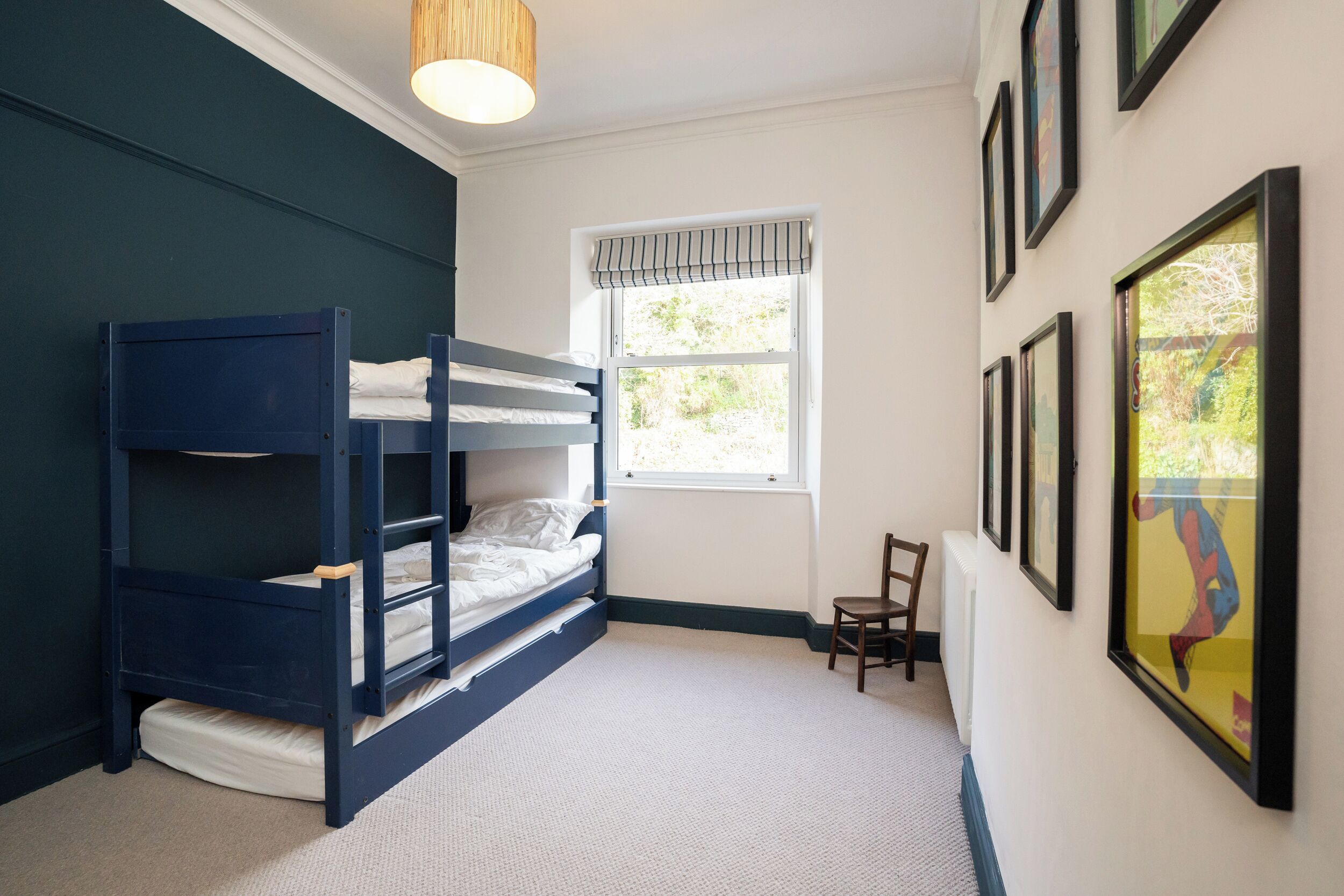 Ein Zimmer mit Etagenbett, einem Fenster mit Jalousien, einem Stuhl und gerahmten Bildern an der Wand.