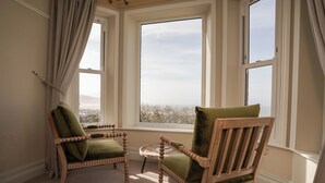 A room with two wooden chairs with green cushions, a small round table, and a view through large windows. - Haulfryn (Barmouth)