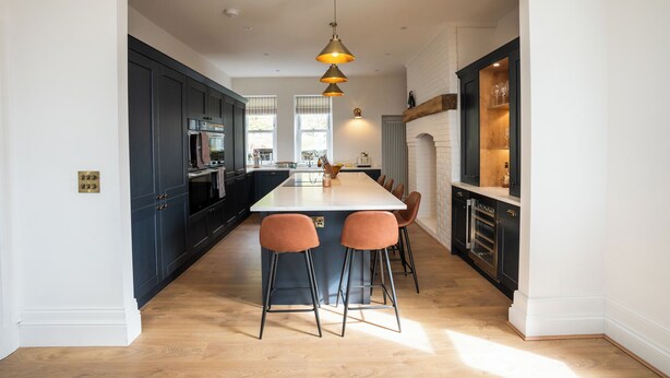 A modern kitchen with dark cabinets, a central island with bar stools, and pendant lighting. - Haulfryn (Barmouth)