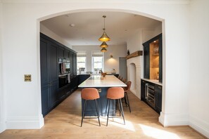 A modern kitchen with dark cabinets, a central island with bar stools, and pendant lighting. - Haulfryn (Barmouth)